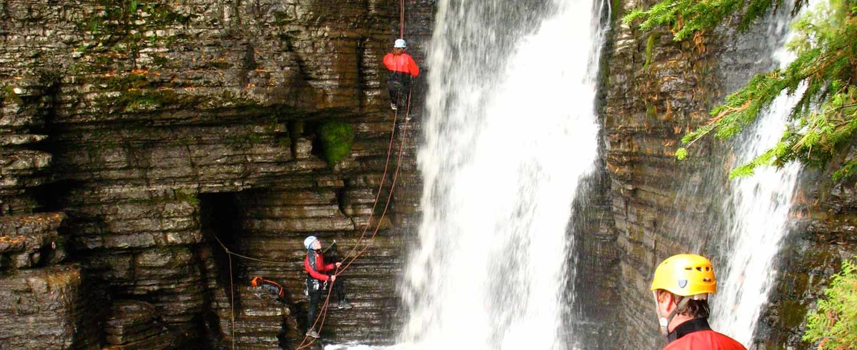 Des participants en casque descendent en rappel à côté de la chute Jean-Larose