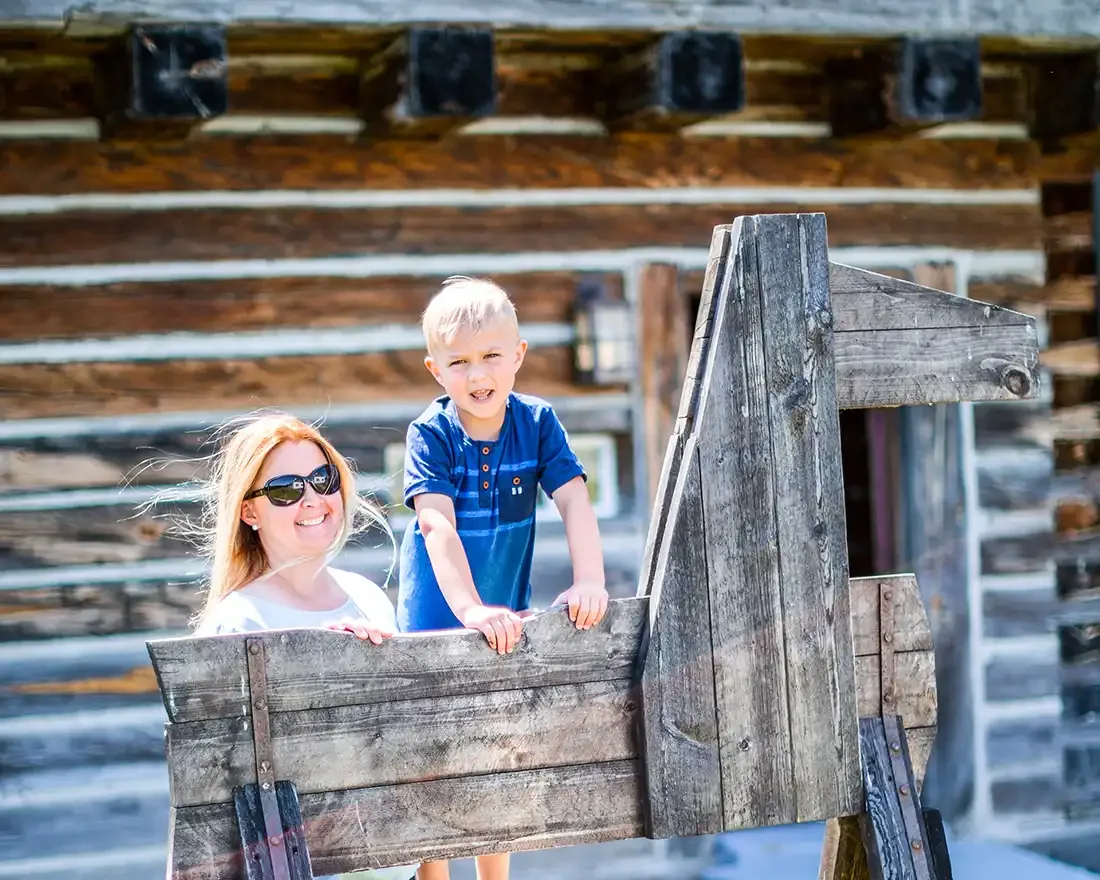 Un enfant et un adulte explorent une installation en bois devant un bâtiment du Fort Ingall